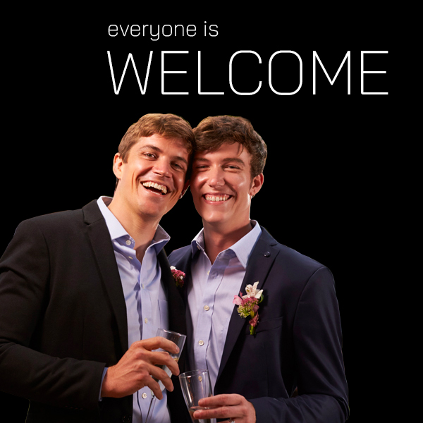 Title: Everyone is Welcome. Image of two gay men hugging while holding wine glasses.
